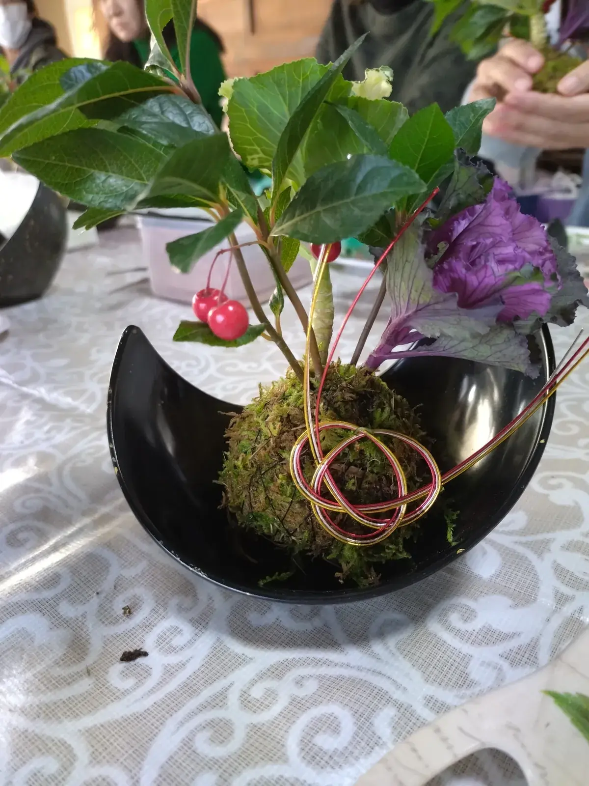 三日月形の黒い器に、苔玉と葉や実、水引をあしらった小さな正月飾り