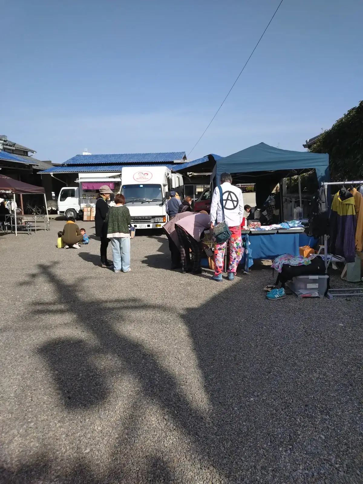 砂利の庭に張られたテントと、遠くに古民家が見えるフリーマーケットの全景