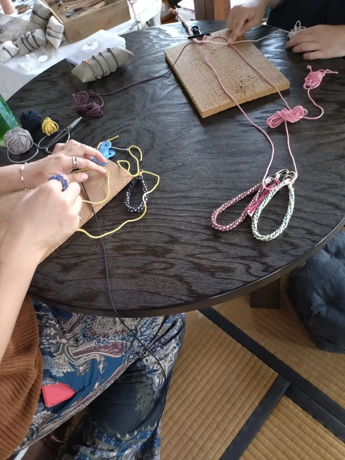座卓の上で、ピンクや黄色の紐を編む手元