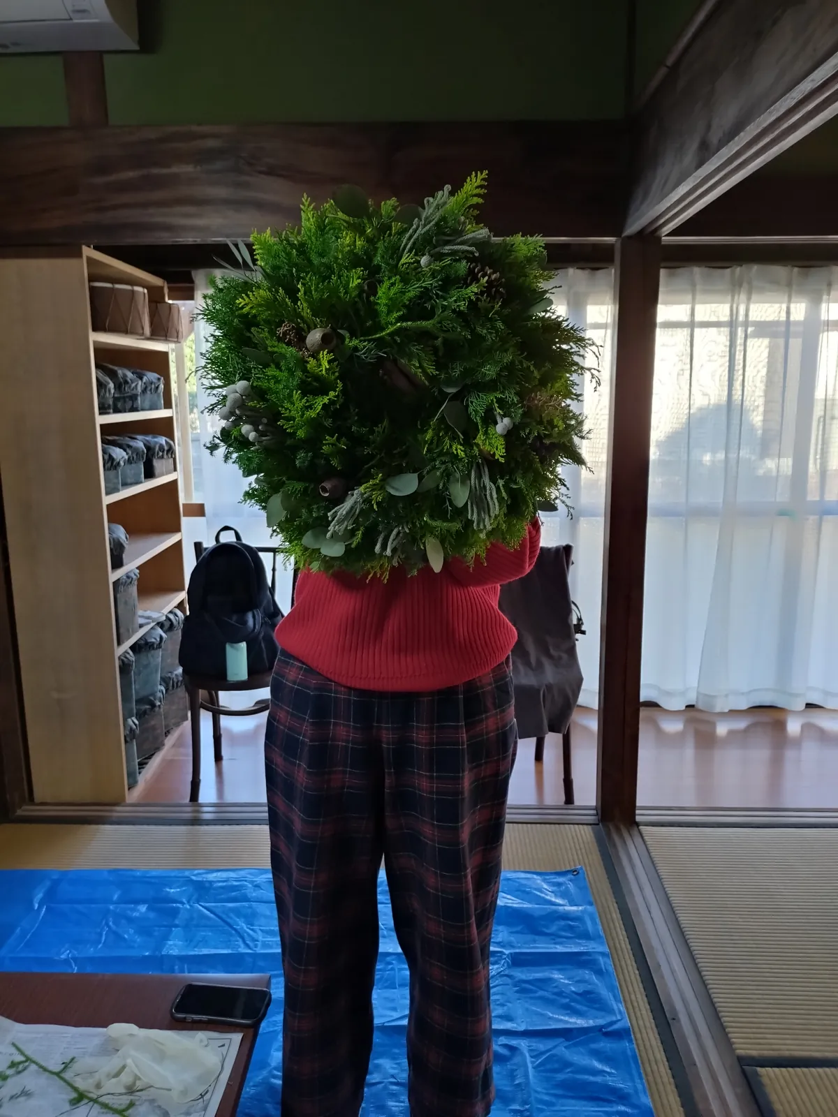 出来上がったリースを胸の前で抱える人（顔はリースで隠れている）
